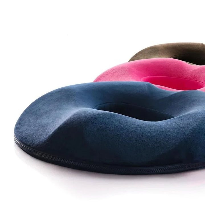 Orthopaedic seat cushion in navy, pink, and brown showing donut-shaped design with central opening for coccyx relief