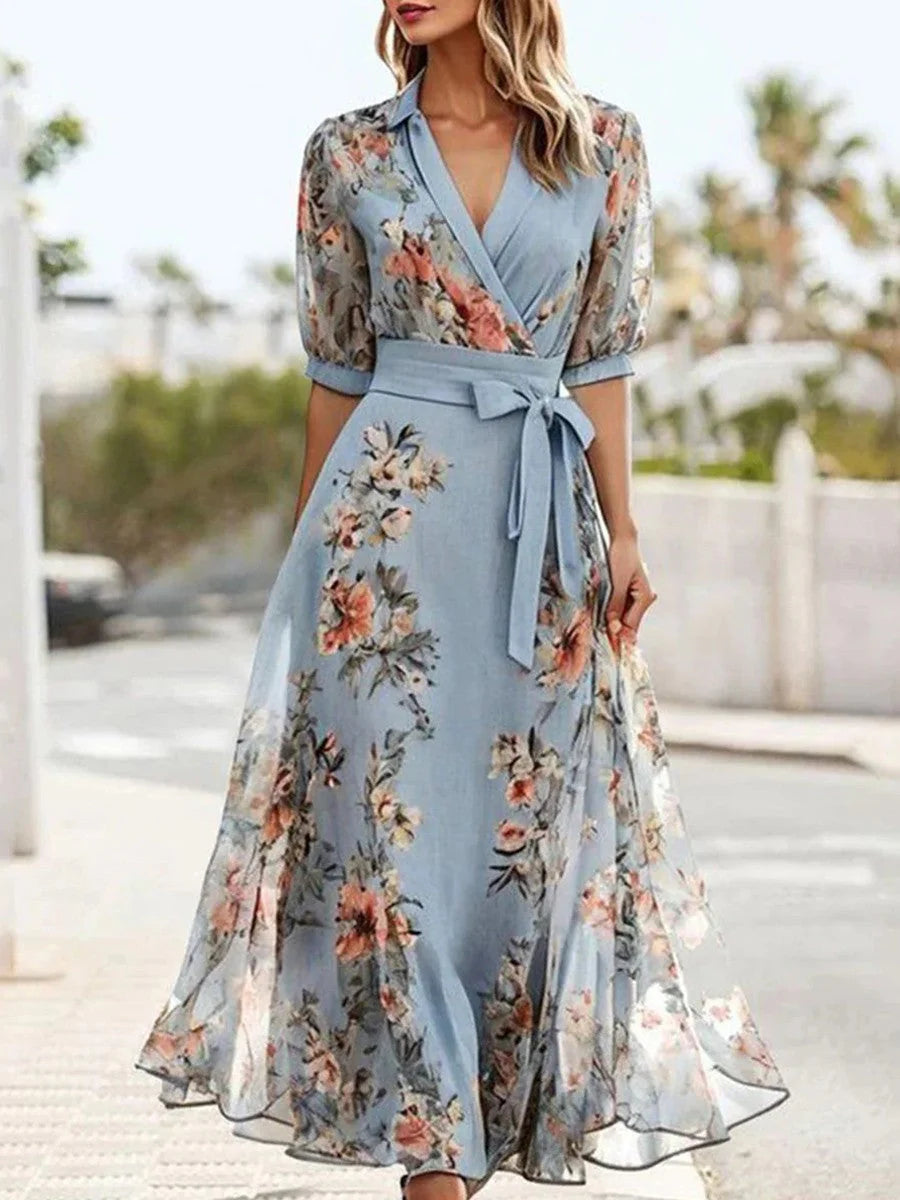 Floral midi dress with wrap V-neckline, sheer floral sleeves, tie waist belt, and flowing skirt in soft blue tones