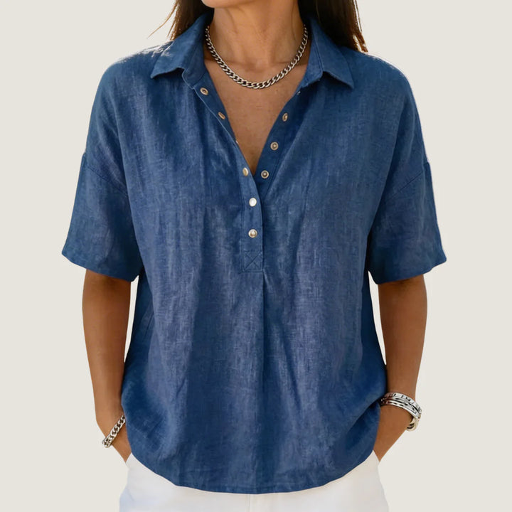 Woman wearing a blue casual button-up collar shirt with short sleeves and relaxed fit, styled with white trousers