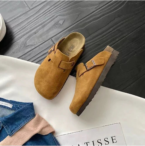 Close-up of tan suede clogs showing adjustable metal buckle and closed-toe design