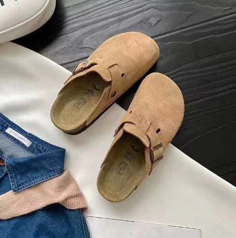 Women's suede clogs styled with denim jeans on neutral background