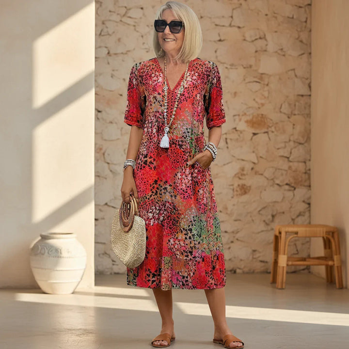 Woman wearing vibrant printed V-neck midi dress with abstract coral and teal pattern in sunlit courtyard