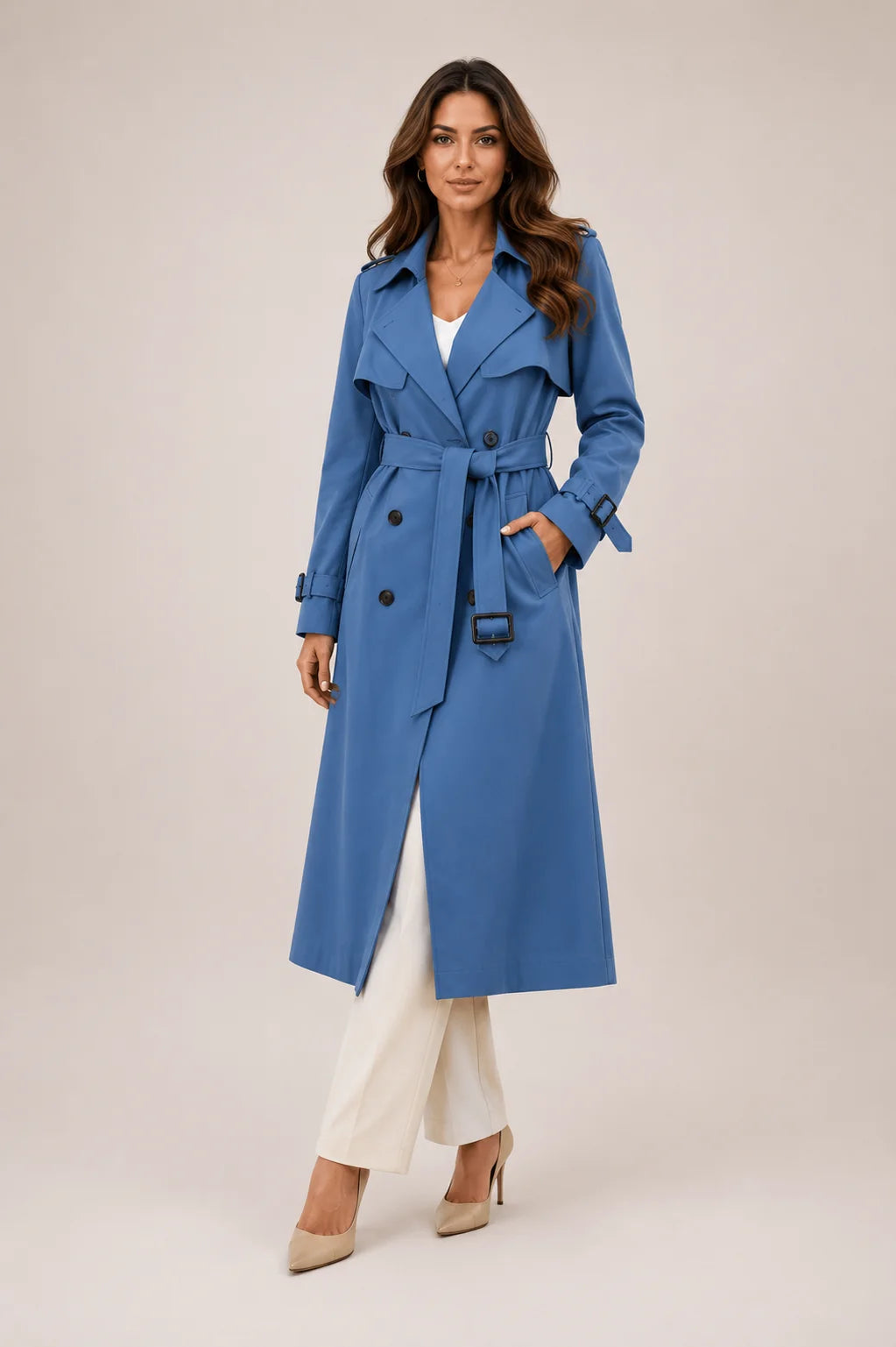 Beige longline trench coat with notched lapels and buckled cuffs worn with tailored trousers