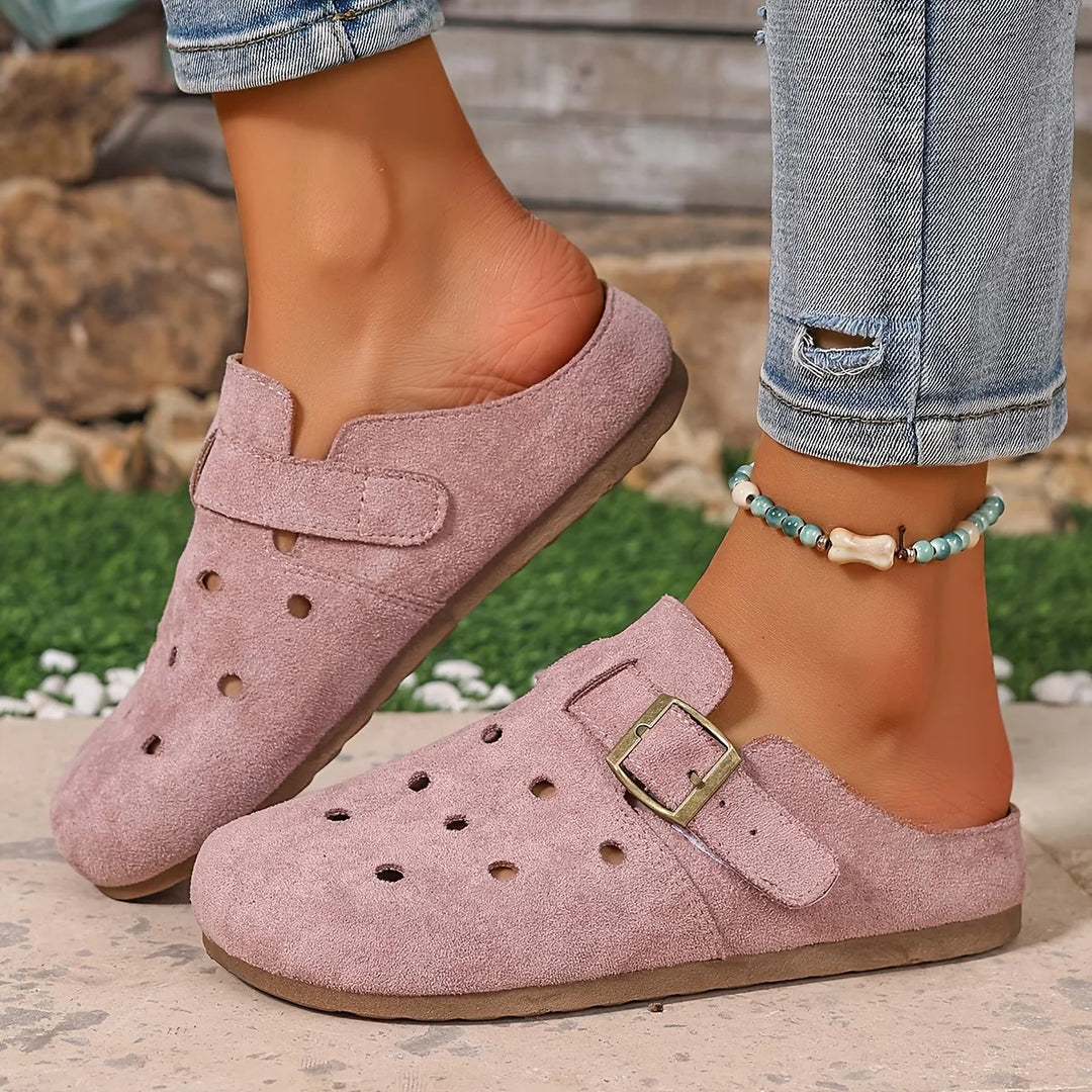 Side profile of beige clogs with hook-and-loop heel strap worn with cropped denim jeans outdoors