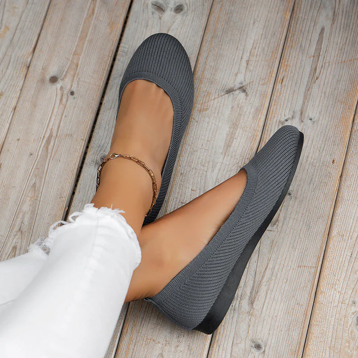 Women's knit slip-on flats in grey with ribbed textile upper and slip-resistant sole on wooden floor