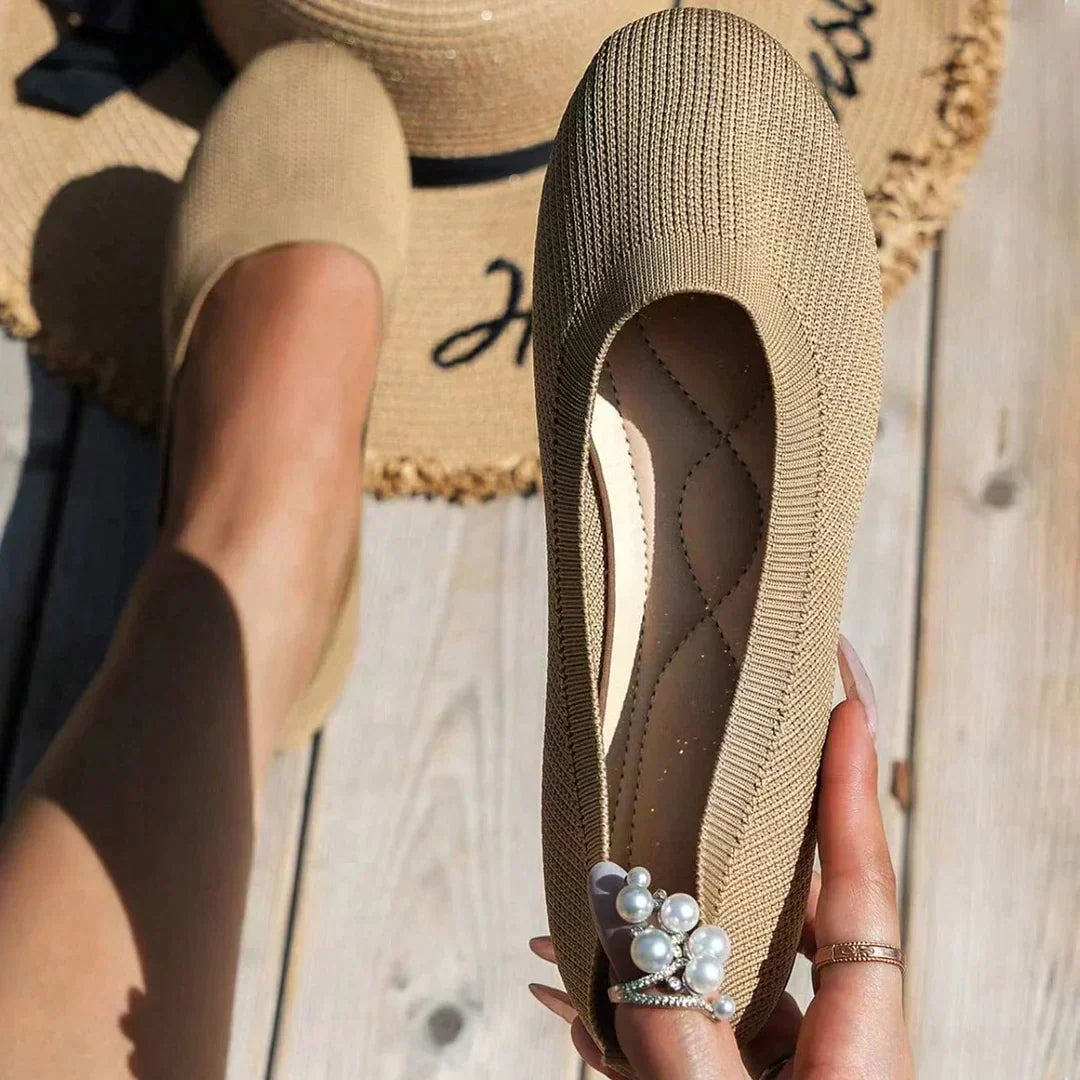 Women's grey knit flats worn with white trousers showing slip-on construction and comfortable fit