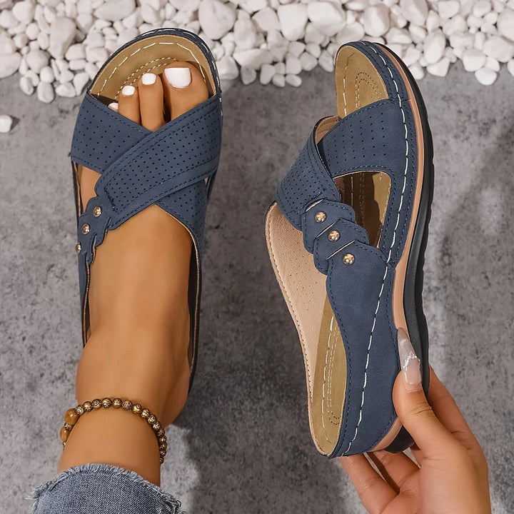Women's wedge sandals with crossover straps and perforated upper in navy blue, styled on foot