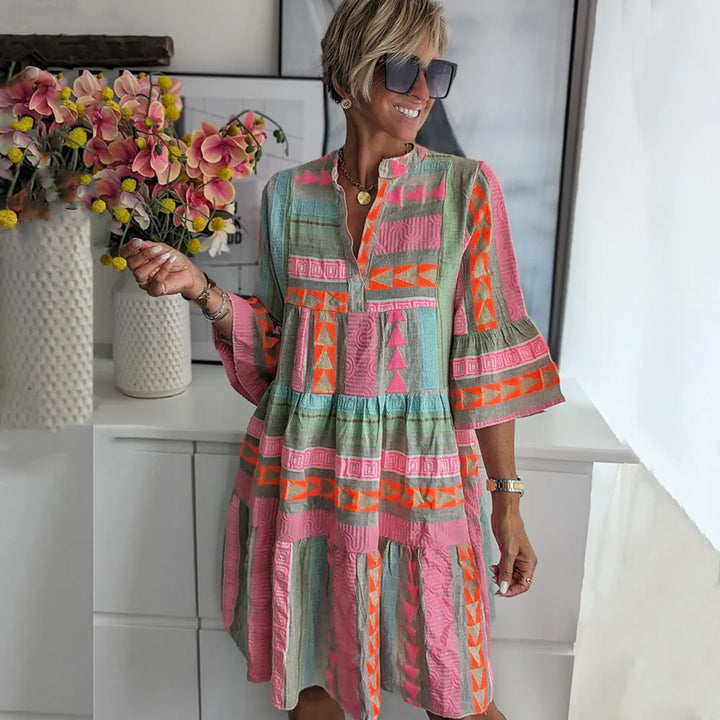 Tiered swing midi dress with vibrant geometric print in coral, pink, and sage tones worn with sunglasses