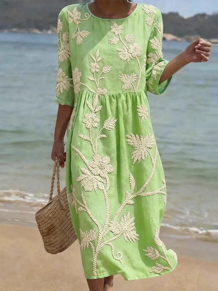 Full-length view of embroidered floral midi dress worn with woven bag on beach setting