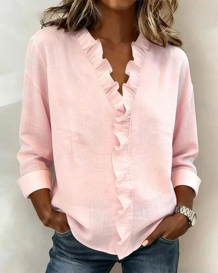 Women's ruffle neck blouse in pink with V-neckline and long sleeves, styled with denim jeans