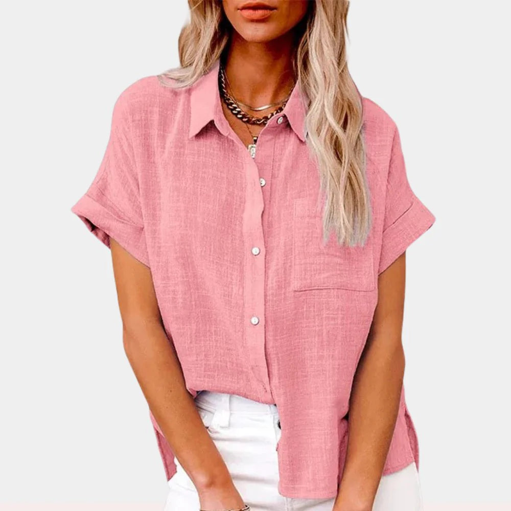 Woman wearing a relaxed-fit pink button-front shirt with short sleeves and chest pocket, styled with white trousers