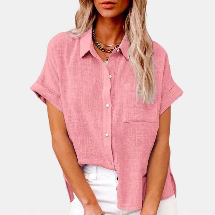 Woman wearing a relaxed-fit pink button-front shirt with short sleeves and chest pocket, styled with white trousers