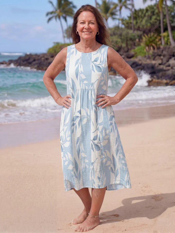 Woman wearing a sleeveless midi dress with botanical print and gathered waist on a tropical beach.