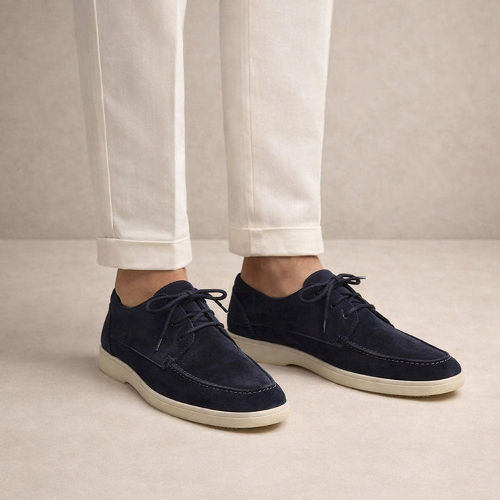 Men's lace-up moc-toe shoes in navy, worn on model with cream trousers