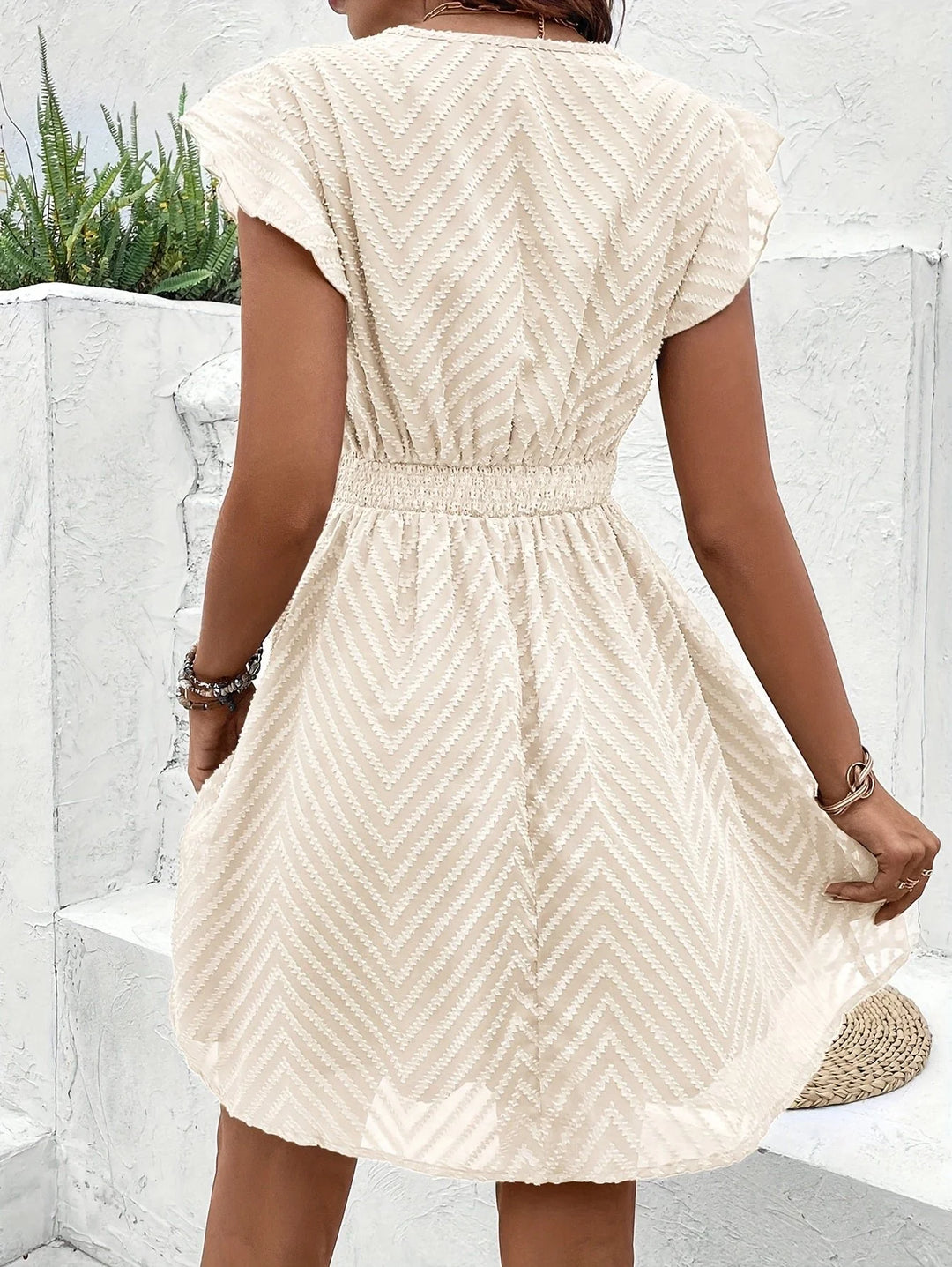 Detail of chevron-textured fabric and crochet lace waistband on cream mini dress
