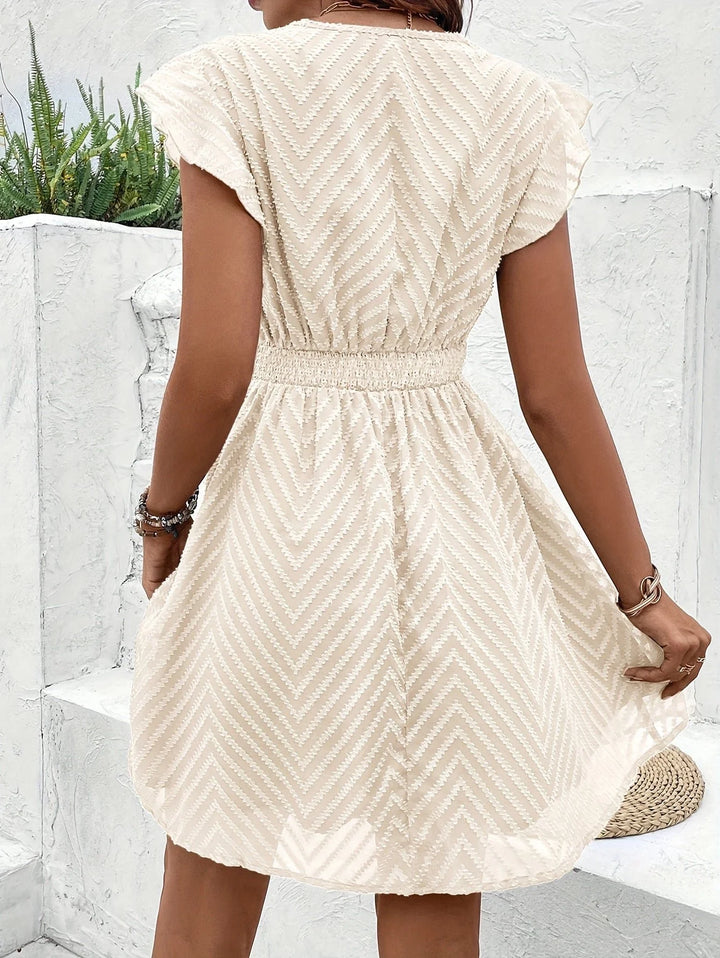 Detail of chevron-textured fabric and crochet lace waistband on cream mini dress