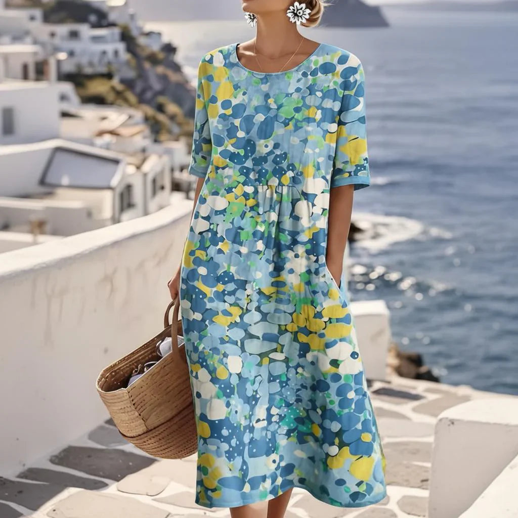 Woman wearing abstract print midi dress with blue floral pattern and gathered waist by the coast