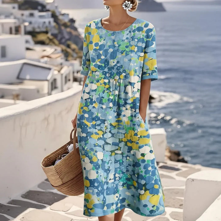 Woman wearing abstract print midi dress with blue floral pattern and gathered waist by the coast