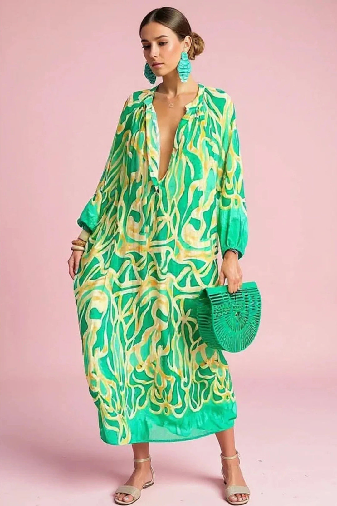 Woman wearing abstract print kaftan maxi dress with bold green and yellow swirl pattern and deep V-neckline