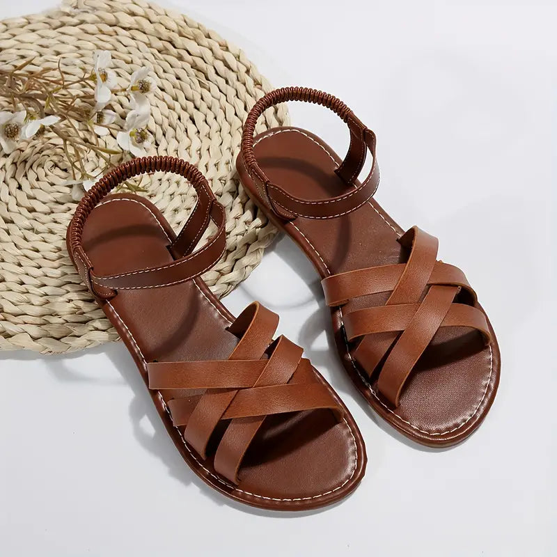 Women's strappy flat sandals in brown with woven crossover straps and elasticated ankle strap on wicker mat