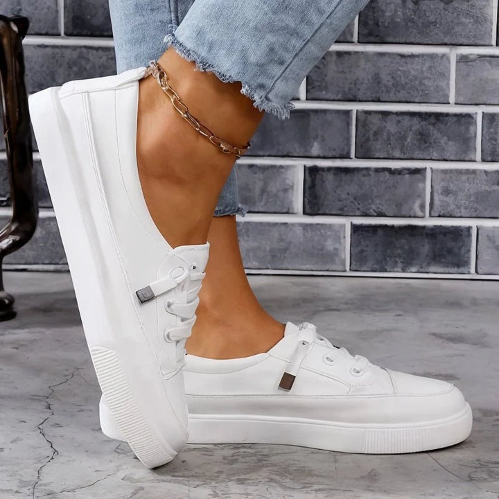 Close-up view of white lace-up trainers showing smooth upper construction and structured design with arch support