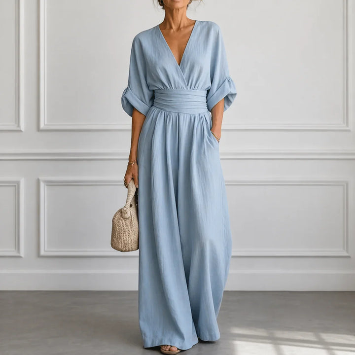 Model wearing light blue wide sleeve jumpsuit with woven basket bag